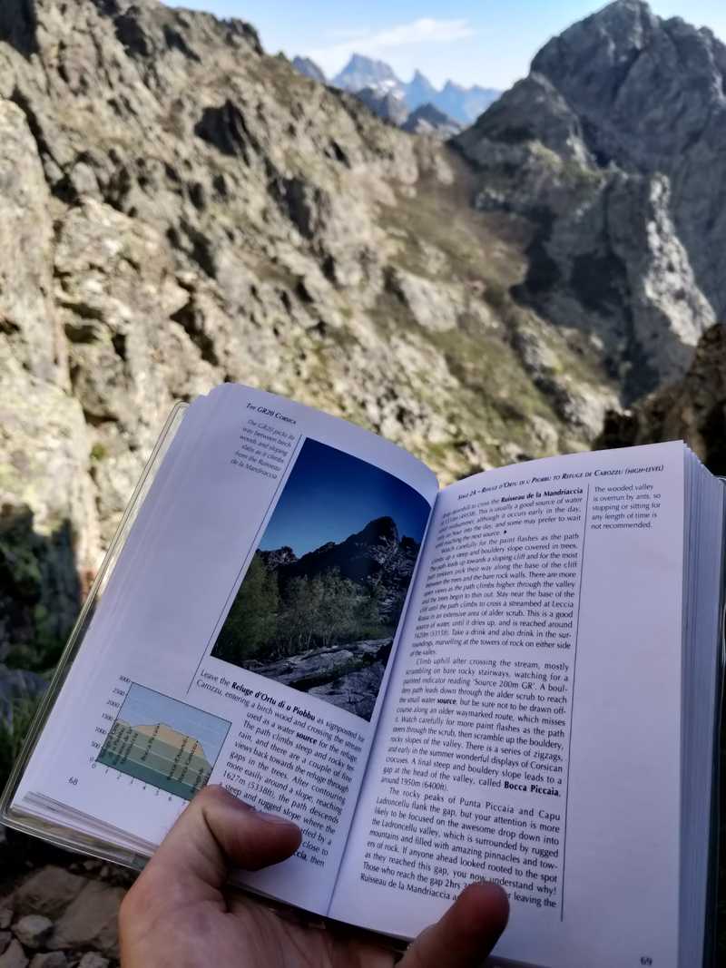 me reading the GR20 Corsica stage guidebook with a mountain backdrop behind me
